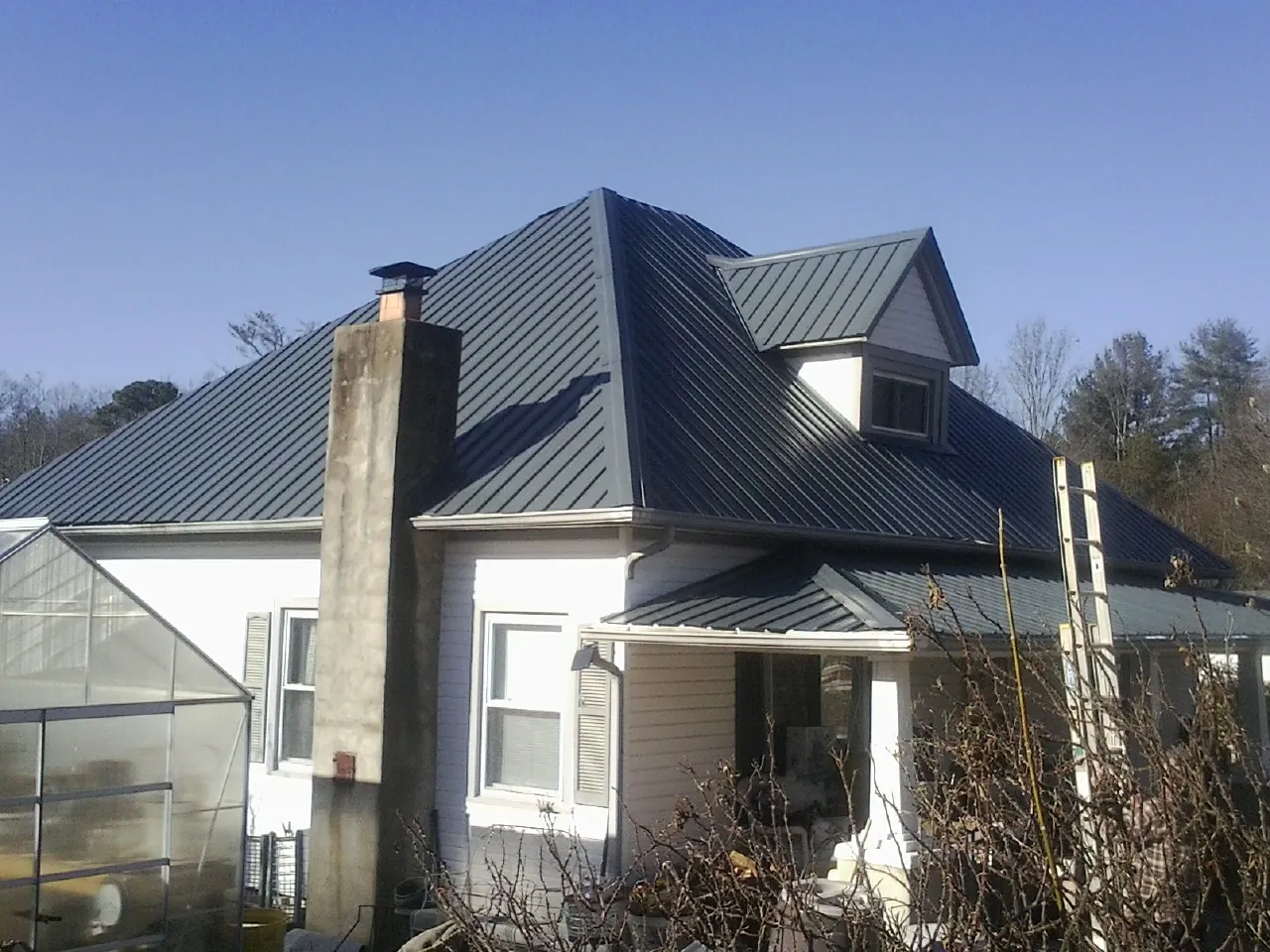 Dark blue standing seam metal roof on a white farmhouse with dormer — Slate & Tile Roof Repair by Roofing Brothers in Brooksville