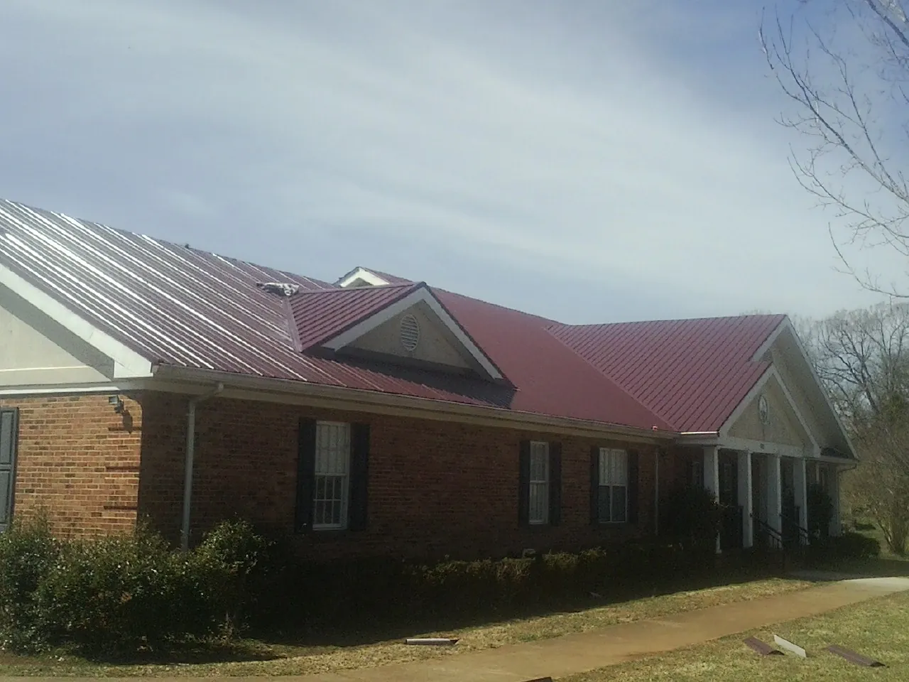 Red metal roof with gabled entries on a long brick building, from a Hail Damage Roof Repair job in Brooksville