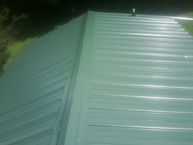 New green metal panels meeting at the ridge of a roof — Flat Roof Repair work by our crew in Brooksville
